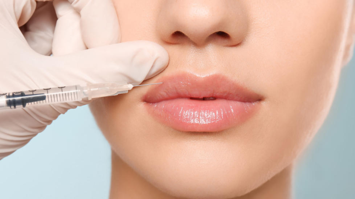 Young woman getting lip injection on color background, closeup
