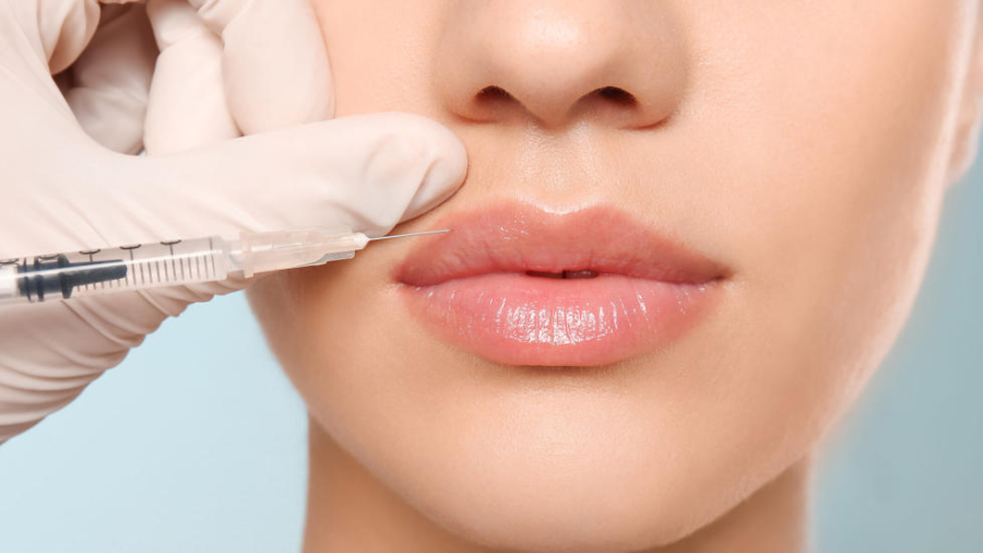 Young woman getting lip injection on color background, closeup